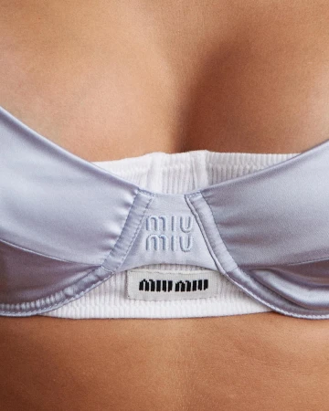 Close-up of a light blue satin bra with white ribbed trim, featuring the MIU MIU logo embroidered on the front, fashion, apparel.