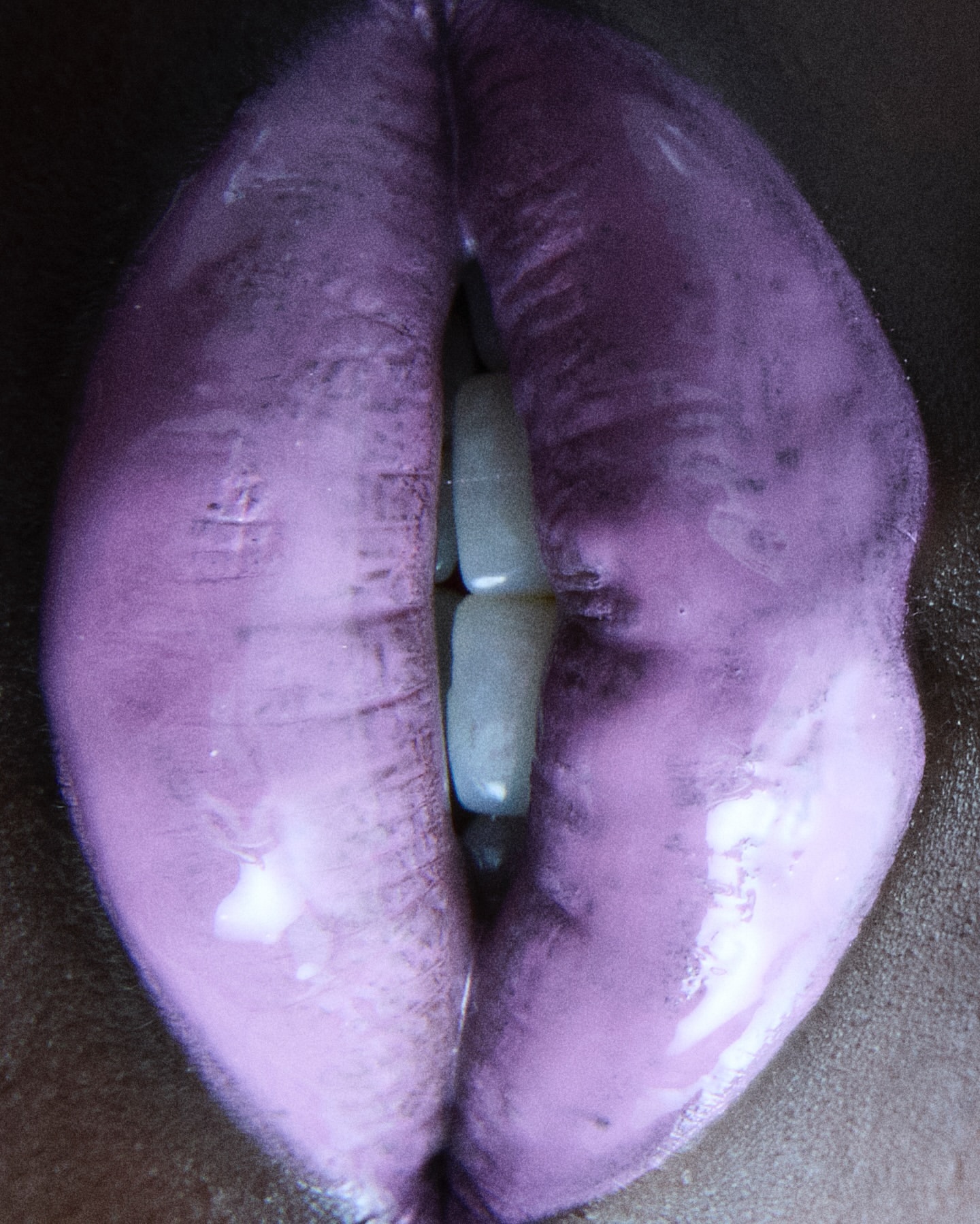 Close-up shot of human lips covered in a glossy, light purple lipstick, revealing a glimpse of white teeth, creating a bold beauty statement.