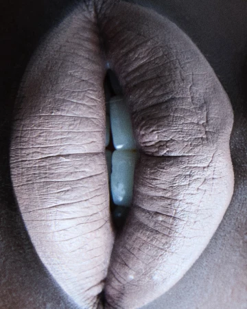 Extreme close-up macro view of lips parted slightly to reveal white teeth, photographed in Paris by Jeanne Lucas.