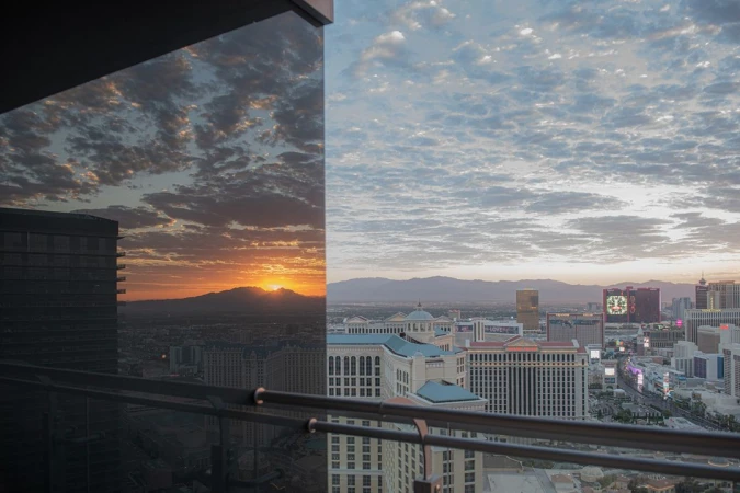 Las Vegas cityscape featuring hotel buildings, the sunrise, and distant mountains, captured from a high-angle perspective.