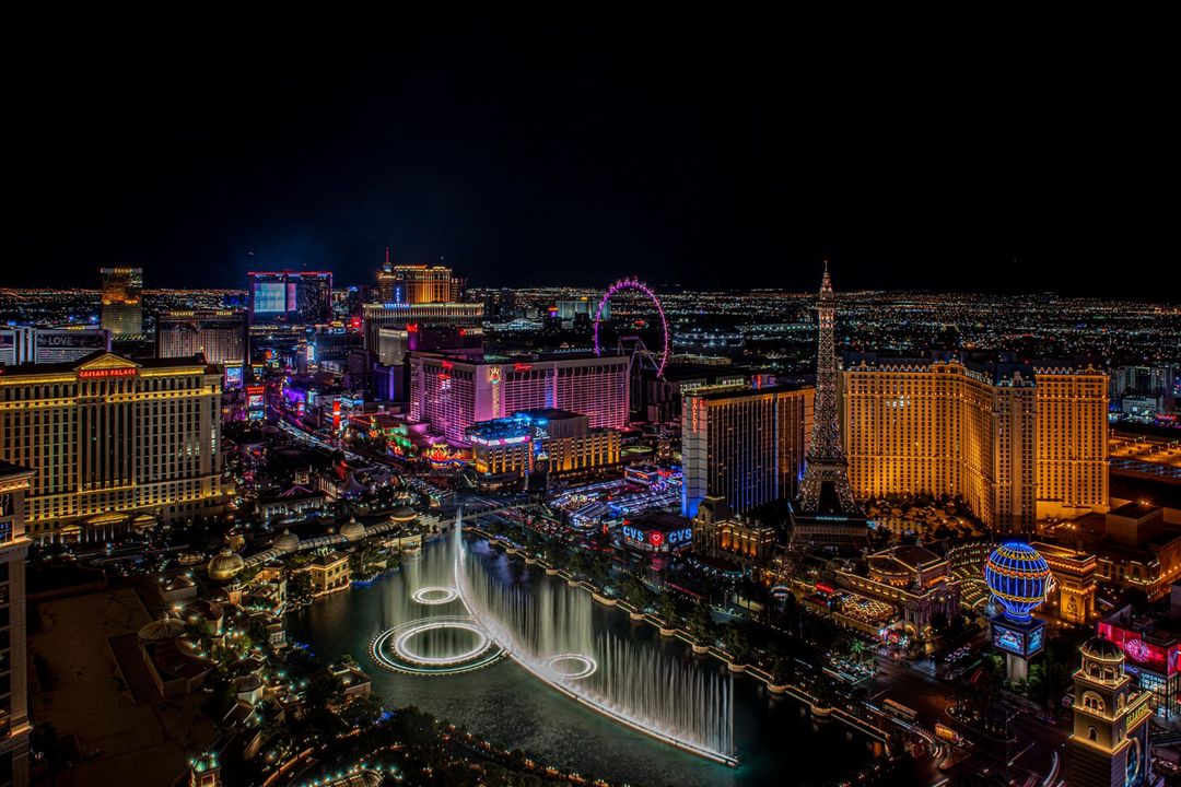 Nighttime cityscape view of the illuminated Las Vegas Strip with hotels, casinos, and the Bellagio fountains in the foreground.