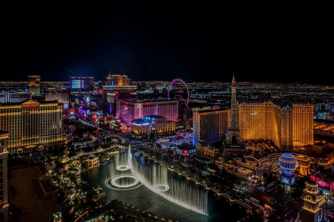 Nighttime cityscape view of the illuminated Las Vegas Strip with hotels, casinos, and the Bellagio fountains in the foreground.