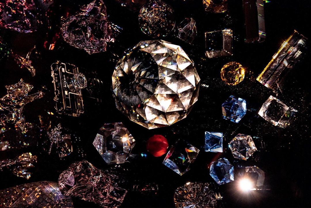 A collection of differently cut and colored diamonds and geometric shapes on a dark surface, creating a glittering, abstract composition.