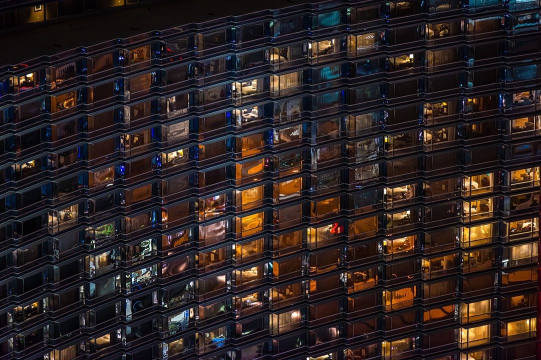 Night view of a high-rise building with many illuminated windows reflecting different interior spaces. 