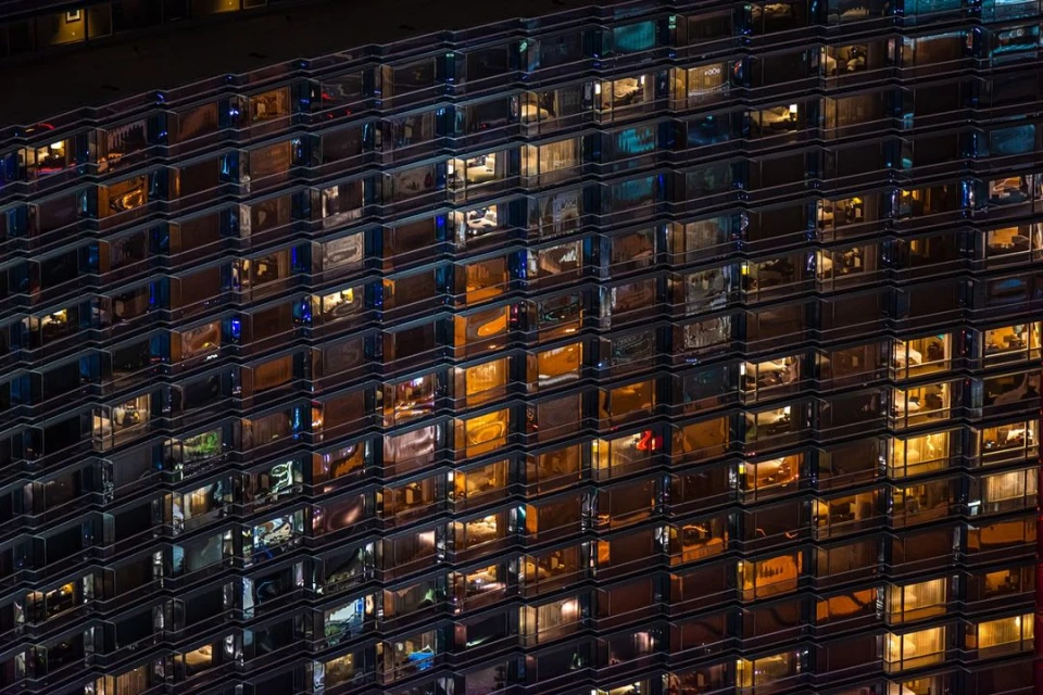 Night view of a high-rise building with many illuminated windows reflecting different interior spaces. 