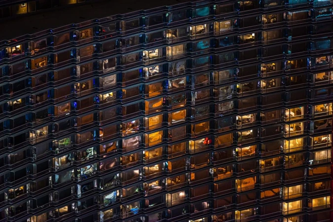 Night view of a high-rise building with many illuminated windows reflecting different interior spaces. 