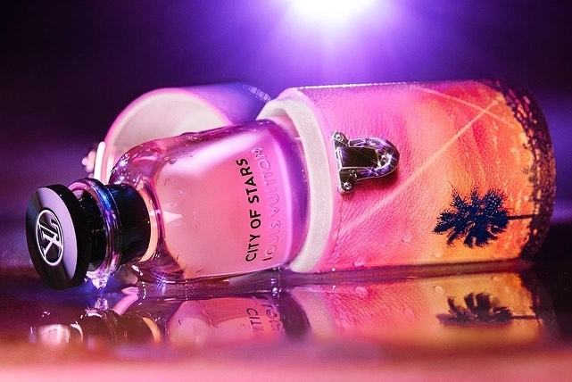 Close-up of a bottle of Louis Vuitton City of Stars perfume with its protective case, resting on a reflective surface with vibrant colors.