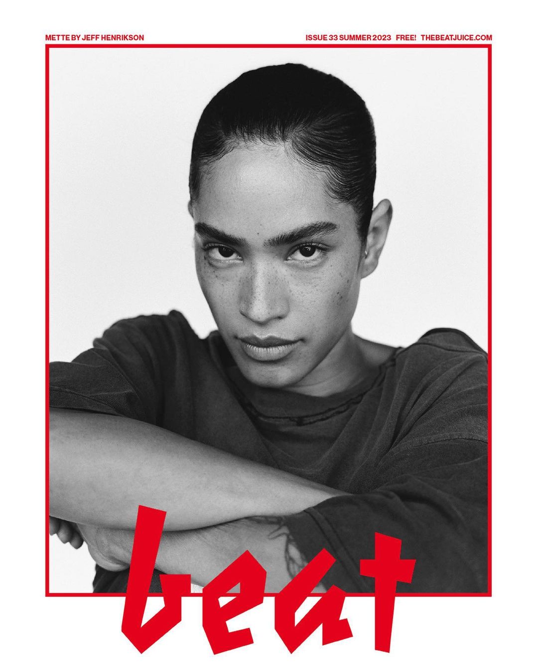 Black and white portrait of a woman with her arms crossed, wearing a dark shirt against a white background with red text.