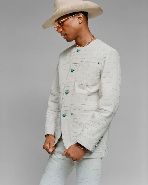 Close-up studio shot of an adult male wearing a straw hat, cream-colored suit, gold chain, and sunglasses, standing in front of a plain grey background.
