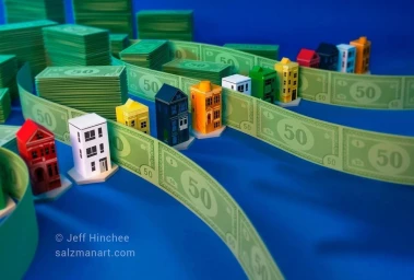 Miniature colorful paper houses arranged along winding paper money ribbons against a bright blue background