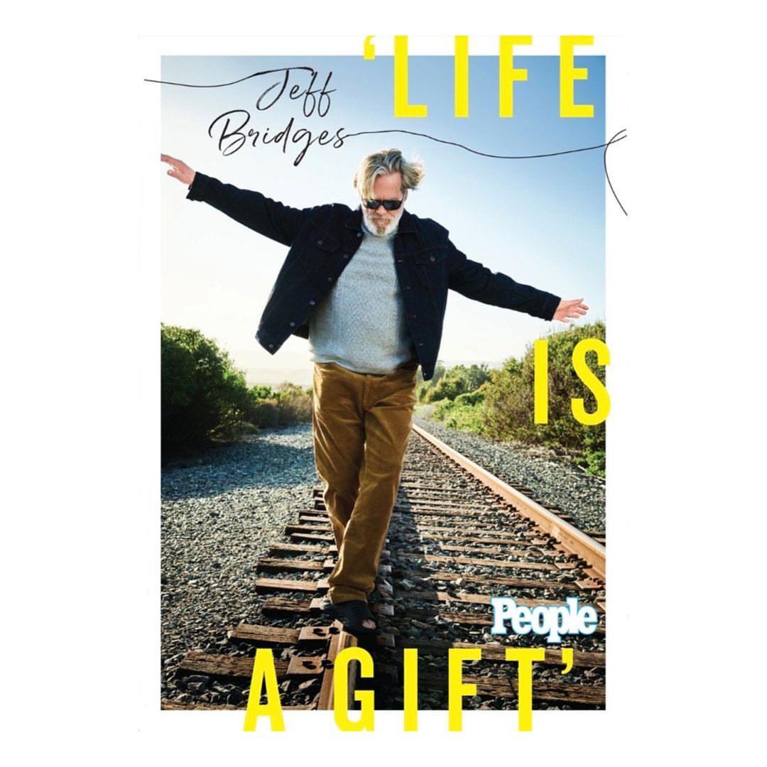 Jeff Bridges balancing on railroad tracks in front of a bright blue sky and green bushes for 'People' Magazine cover.