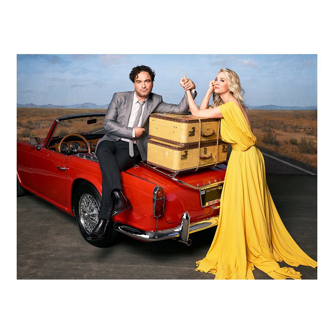 A couple posing on a red convertible car with luggage, set against a desert backdrop under a bright sky, portraying a vintage travel theme.