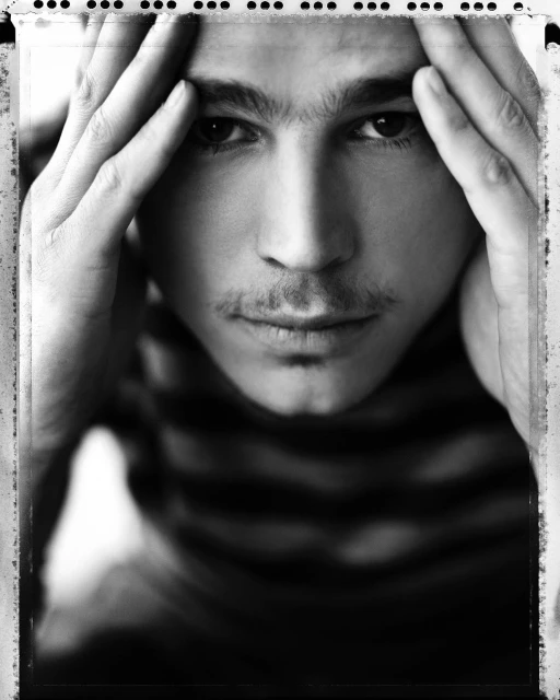 Monochrome portrait of a contemplative adult man with hands near his head, showcasing his facial features and striped shirt.