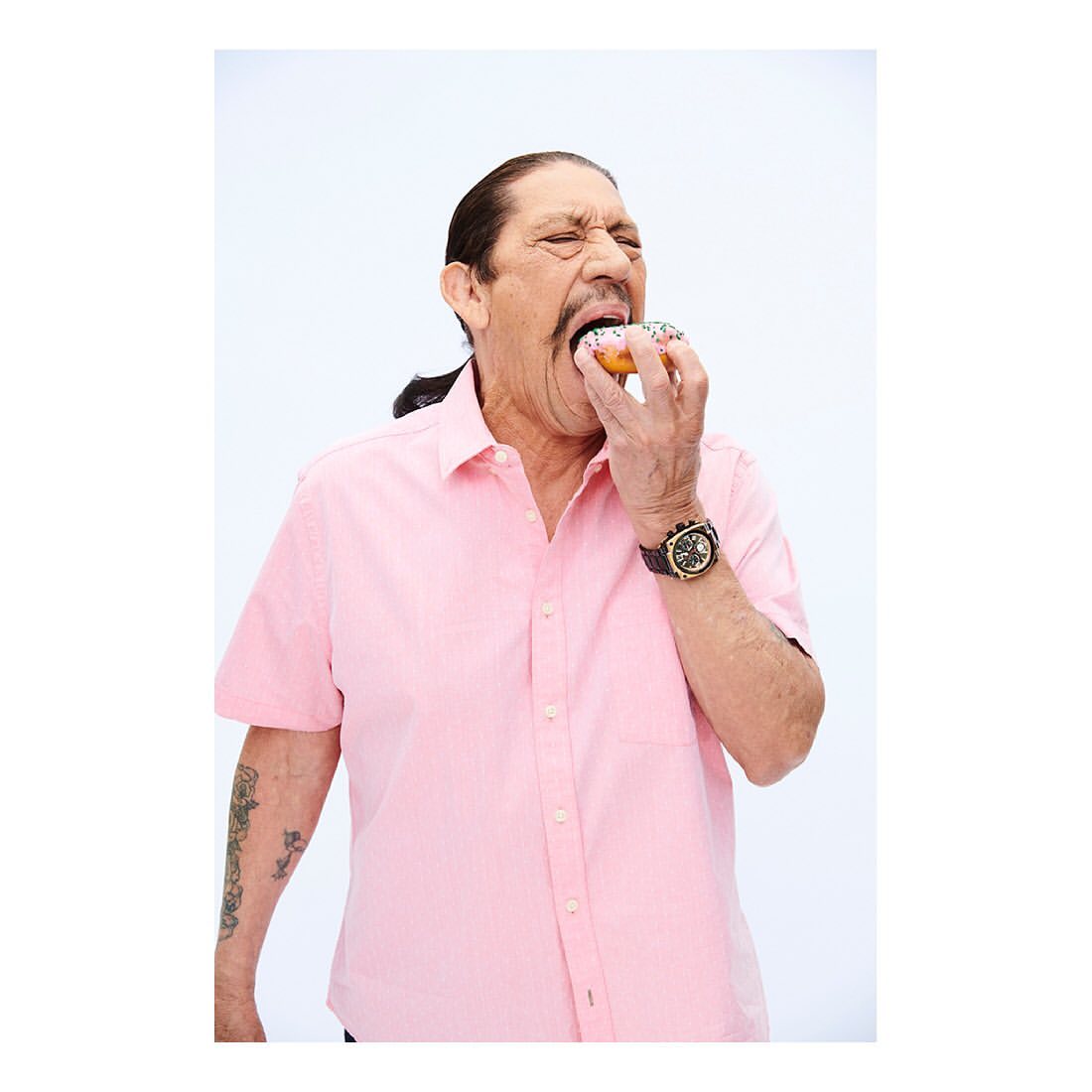 Adult man eating a donut with white frosting and rainbow sprinkles in a studio environment against a white background.