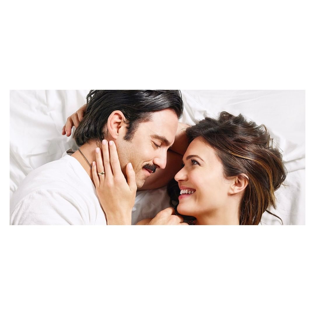 A smiling couple lies face to face in bed, their expressions conveying intimacy and joy, in a close-up shot with soft, natural lighting.