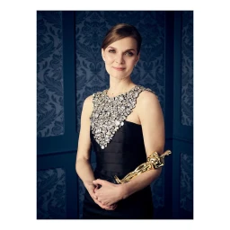 Portrait of a woman wearing a black dress with a heavily embellished jeweled neckline holding an Oscar statuette.
