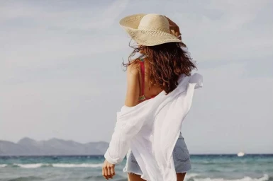 Woman wearing a wide-brim straw hat, white shirt, and denim shorts at the beach by Jeff Luker