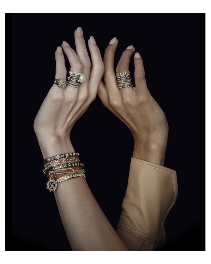 Close-up shot of two hands adorned with rings and bracelets against a black background in a studio. Jewellery fashion shoot.
