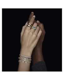 Close-up of interlocking hands adorned with gold rings, diamond bracelets, and gemstone jewelry against a dark background.