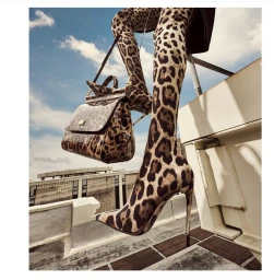 Model wearing head-to-toe leopard print boots and holding a matching handbag on a sunny rooftop by Jeff Stephens