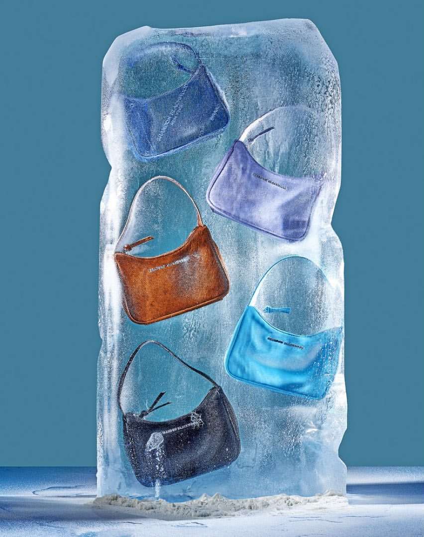 Fashion still life of five colorful leather handbags encased in a large block of ice against a light blue background, studio shot.
