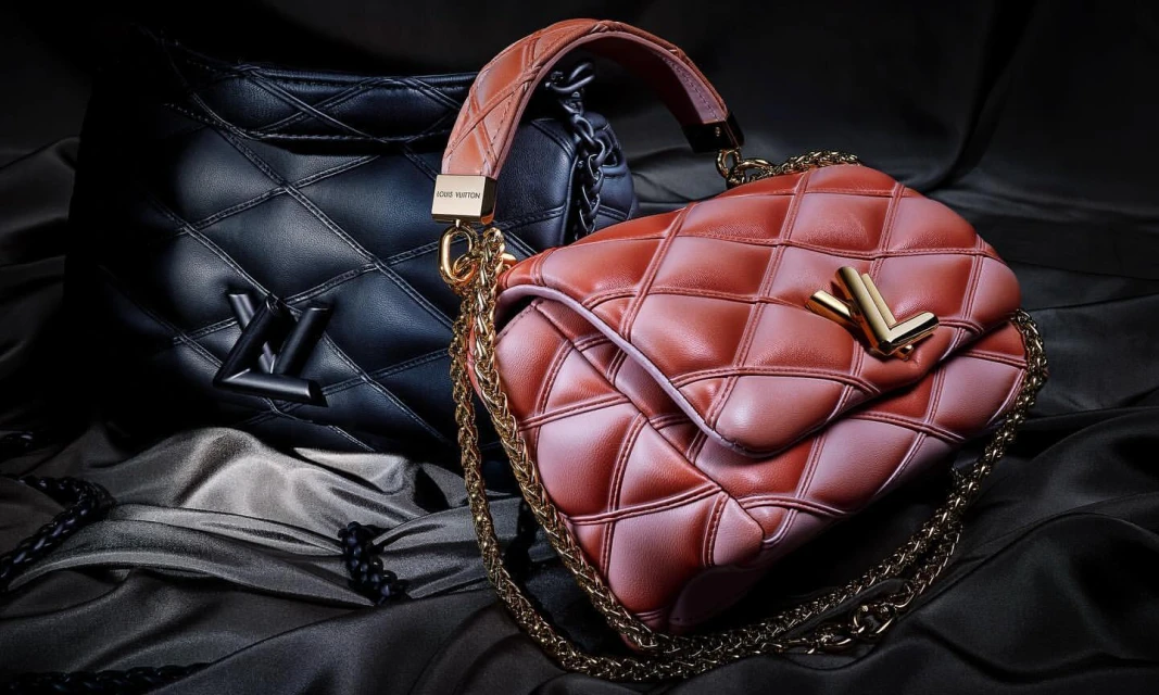 Two quilted leather Louis Vuitton bags, one black and one pinkish-brown, with gold hardware, on a satin black background.