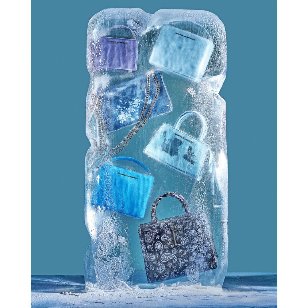 Frozen fashion handbags encased in large ice block against a blue backdrop, cool accessories concept, vivid colour, and crisp details.