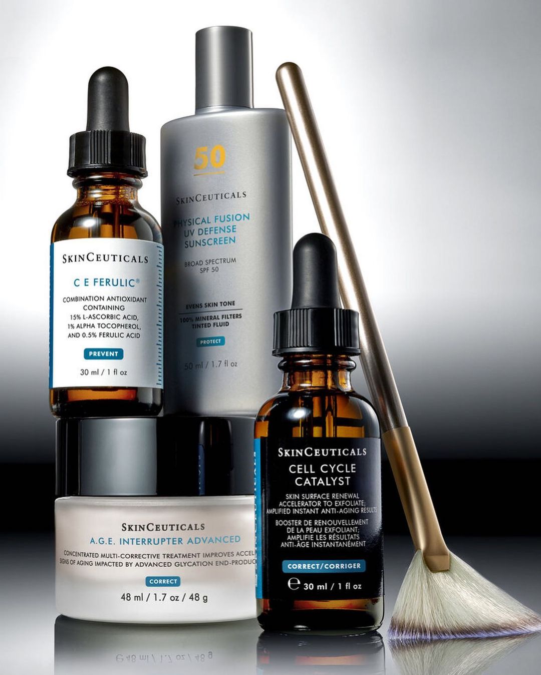 Several SkinCeuticals skincare products including serums, sunscreen, and cream are arranged on a gray surface with a makeup brush.