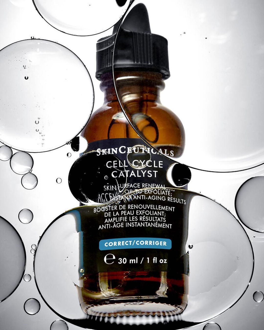 SkinCeuticals Cell Cycle Catalyst bottle with dropper against a bright white background with water droplets for a beauty product shot.
