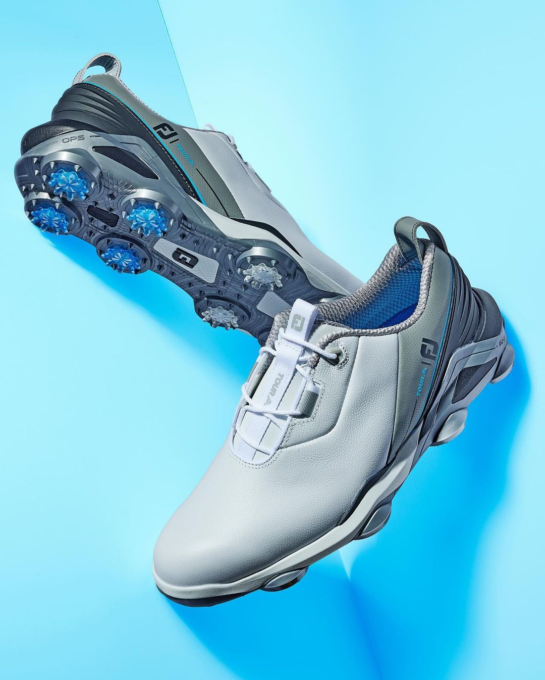 Two FootJoy golf shoes are displayed on a blue surface, one slightly behind the other, showcasing design and construction.