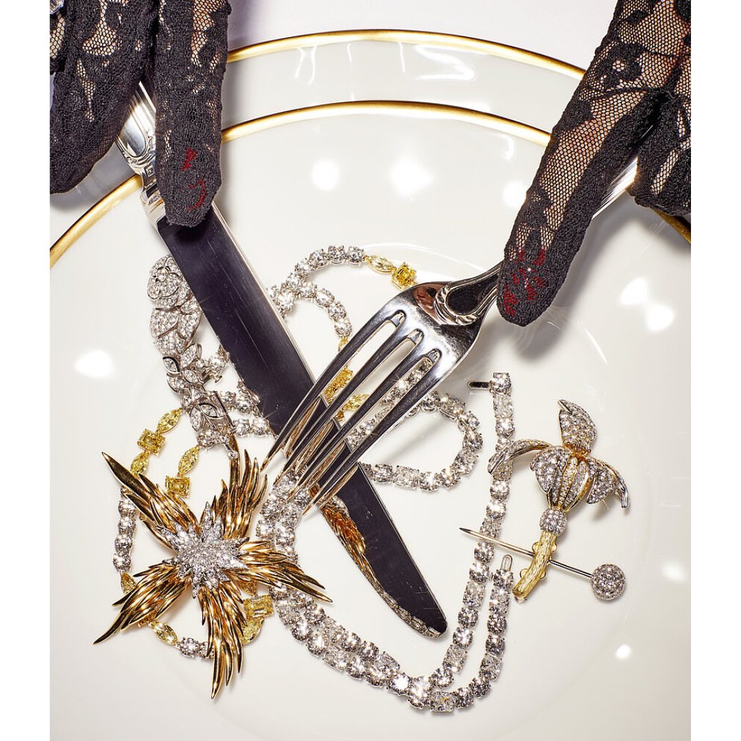 High-angle shot of jewelry displayed on a plate with a fork and knife held by hands in lace gloves, creating a luxury still life.
