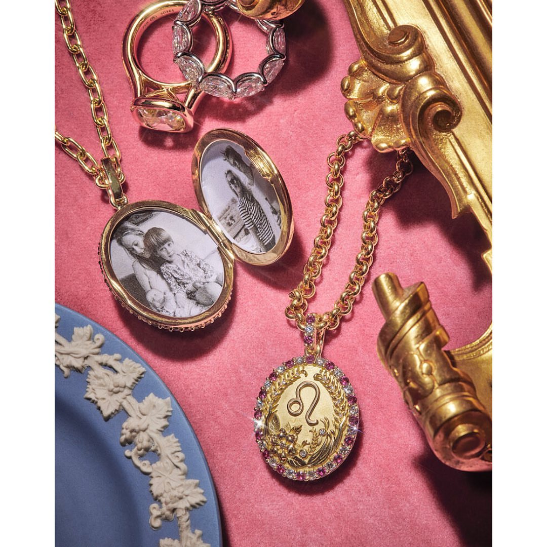 Close-up of gold locket necklaces and rings on a pink surface with a blue plate and gold decoration adding a touch of luxury.