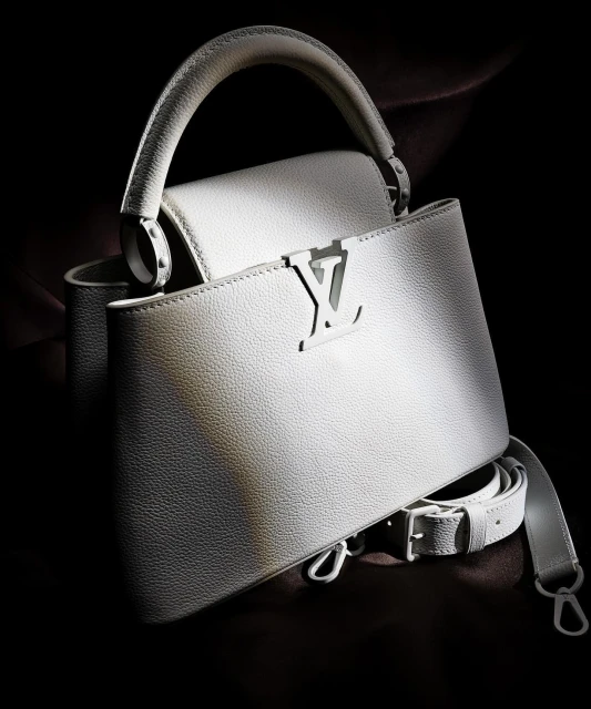 Elegant white leather Louis Vuitton Capucines handbag with top handle and shoulder strap, displayed against a dark background in studio lighting.
