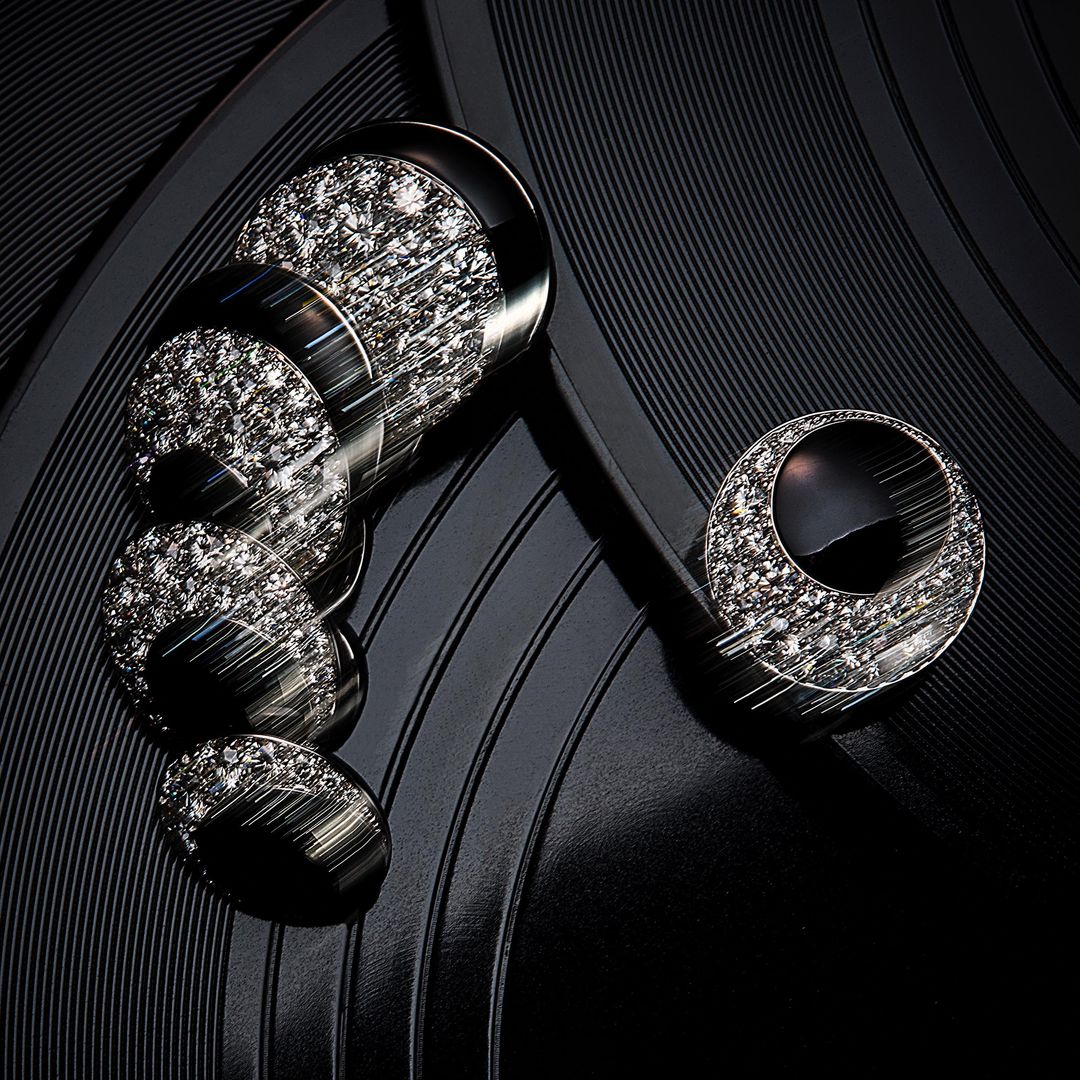 Close-up of black vinyl record featuring musical note-shaped jewelry with diamonds, set against a backdrop of concentric record grooves.