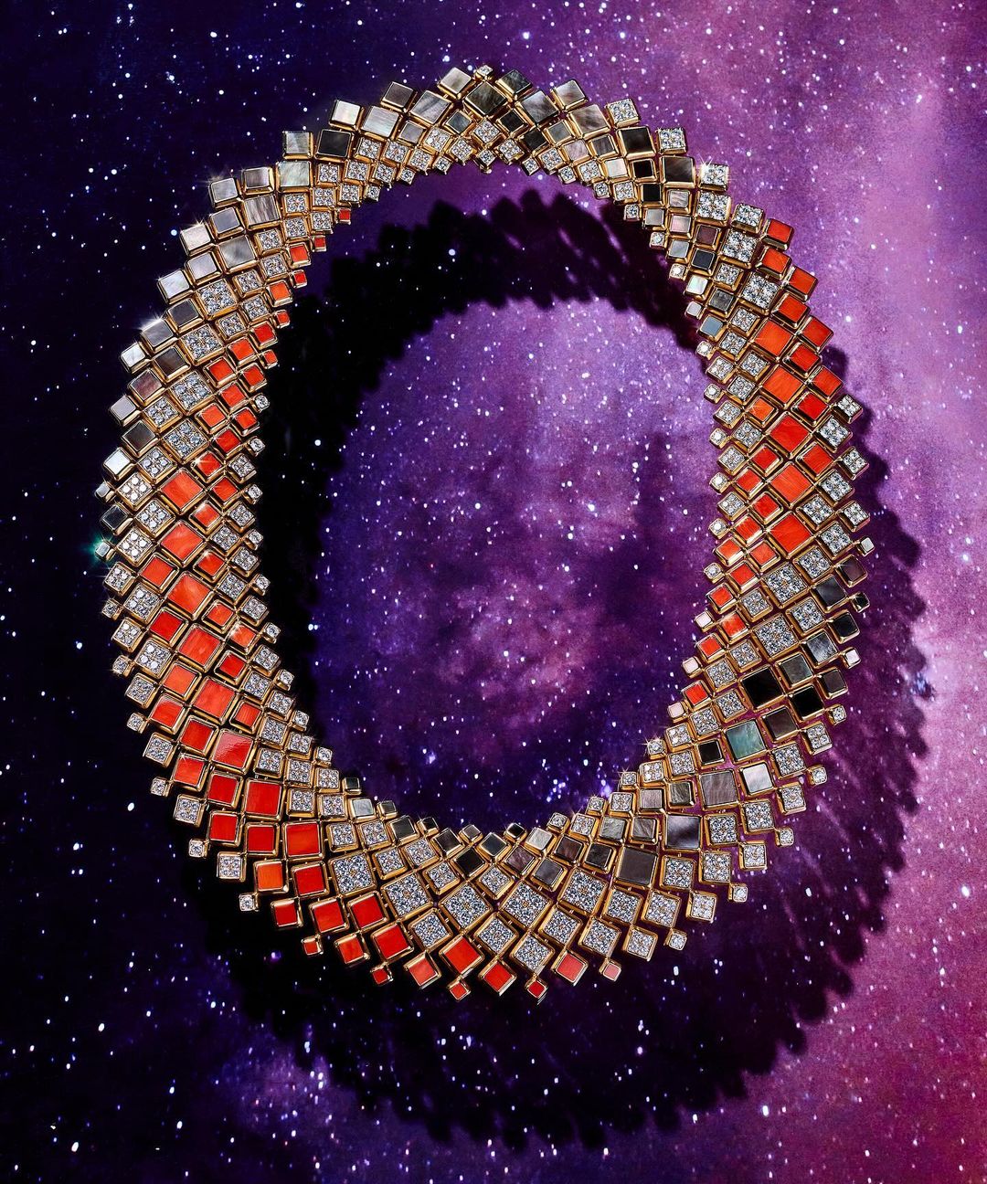 Overhead studio shot of a geometrically complex necklace made of small coral, diamond, and mirror tiles arranged in an open ring.