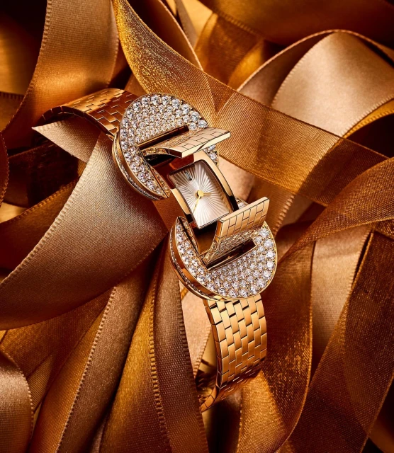 Elegant gold watch with diamond embellishments displayed on a bed of golden ribbons, creating a luxurious and festive visual.