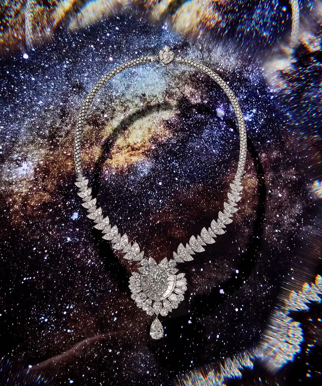 Diamond necklace with a pear-shaped pendant, against a dark cosmic background with white and blue star-like clusters, opulent jewellery.
