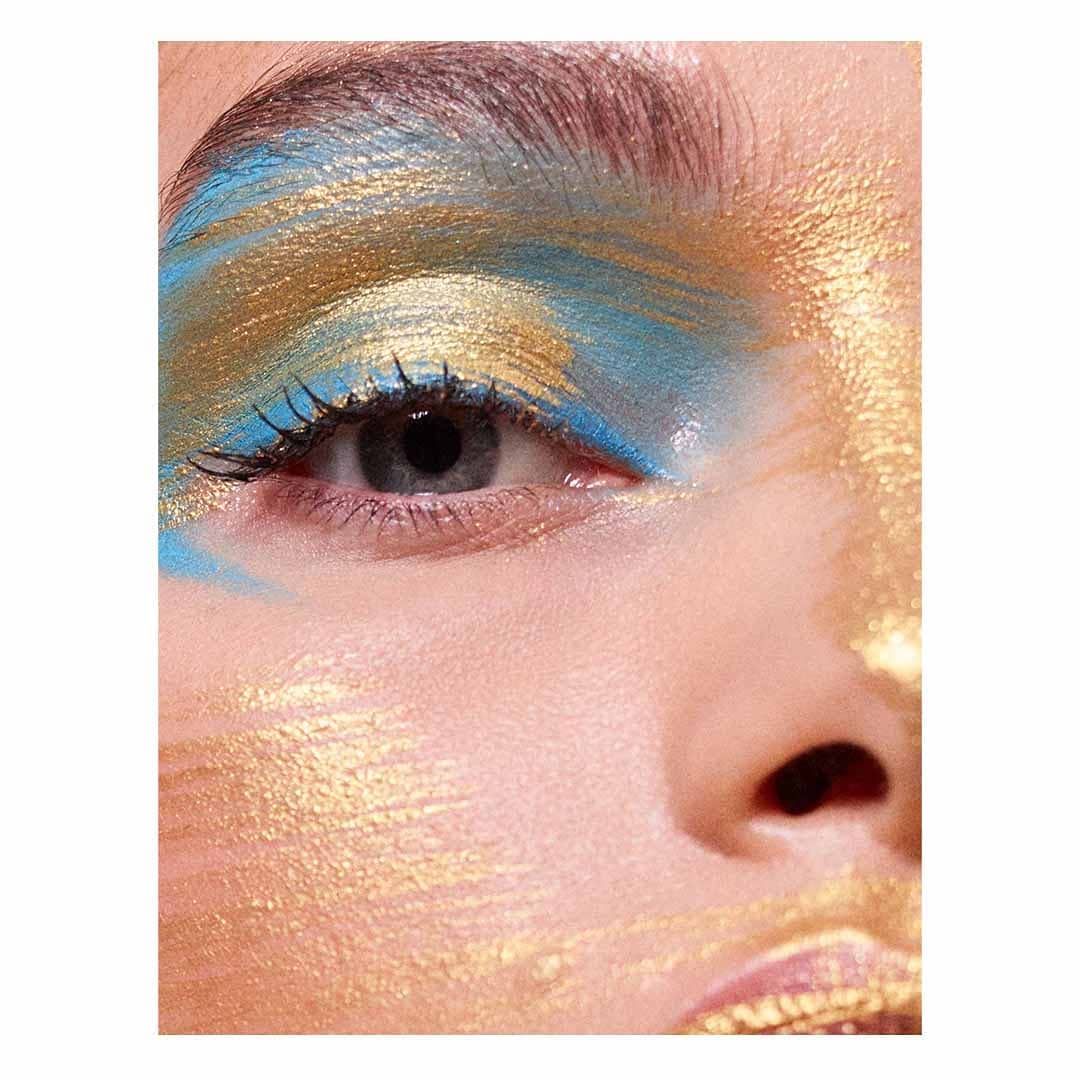 Close-up studio shot of a woman's face with gold and blue eyeshadow and skin highlights for a beauty or cosmetics campaign.