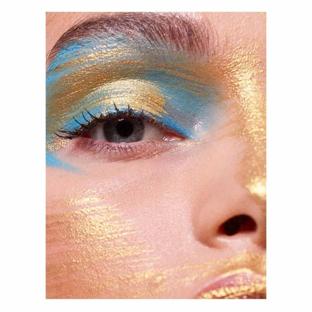 Close-up studio shot of a woman's face with gold and blue eyeshadow and skin highlights for a beauty or cosmetics campaign.