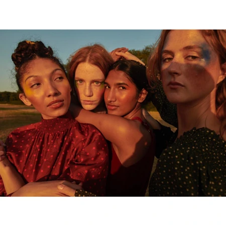 Four women posing closely together outdoors at sunset with warm golden light illuminating their faces and patterned clothing.