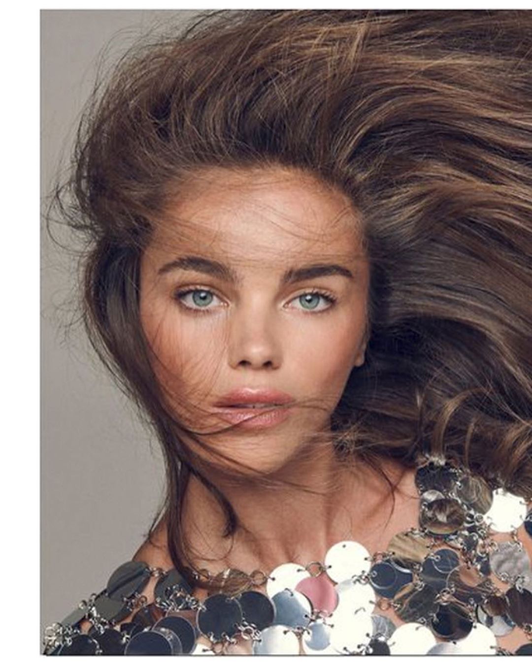 Portrait of a fair-skinned woman with brown hair and blue eyes wearing a metallic silver sequin top, shot in a photo studio.