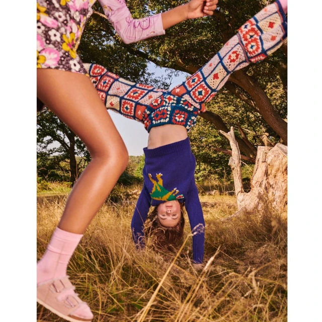 Two children outdoors in a playful pose: one standing with floral print shorts, the other upside down in crochet pants, showcasing a whimsical scene.