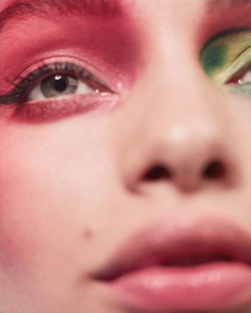 Close-up of a woman's face with vibrant red and green eyeshadow, highlighting the eyes and facial features in a beauty shot.
