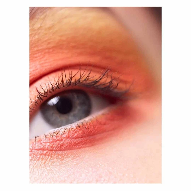 Close-up photo of a human eye with peach-toned eyeshadow on the upper eyelid and lower lashline, emphasizing the detail of the lashes.