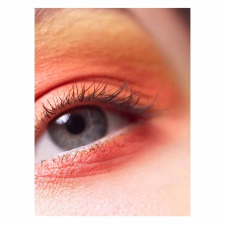 Close-up photo of a human eye with peach-toned eyeshadow on the upper eyelid and lower lashline, emphasizing the detail of the lashes.