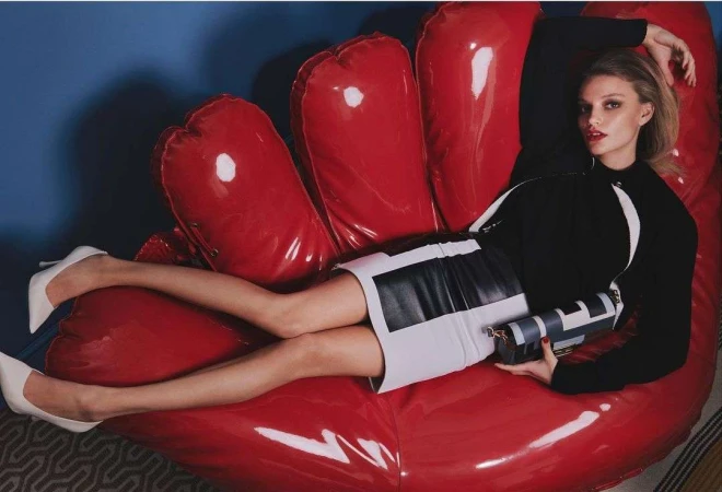 A fashionable adult female model poses reclining on a red inflatable hand wearing a black-and-white skirt and top with white heels.