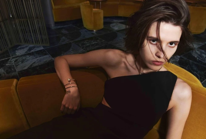 Woman in black dress reclining on gold velvet sofa wearing a gold coiled bracelet