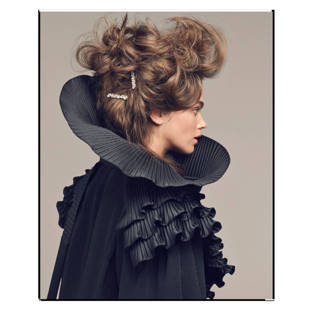 Profile shot of a woman with brown updo and a ruffled, pleated collar against a neutral background in a beauty fashion studio portrait.