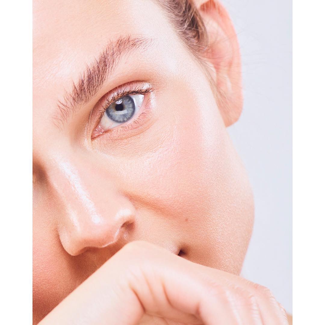 Close-up portrait of a fair-skinned adult female, focusing on her blue eye, flawless skin, and manicured hand near her face.