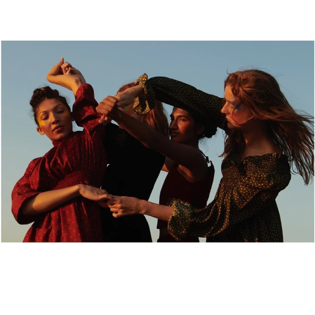 Four women pose together in a natural outdoor setting with golden sunlight, showcasing fashionable dresses in front of a clear blue sky.